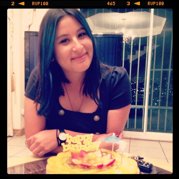 foto de una mujer sonriendo frente a un pastel que tiene un pastel de Feliz cumpleaños